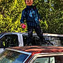 Samuel is registered to the contest to win money with this photo: blue_shirt, bottle, boy, car, casual_clothing, child, daylight, greenery, hair, nature, old_car, outdoor, parked_car, rust, smile, standing, sunlight, trees, van, vehicle