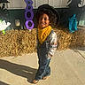 child, boy, cowboy_costume, hat, bandana, overalls, plaid_shirt, smiling, outdoor, halloween, decorations, hay_bale, shadow, concrete, festive, holiday, costume, cute, portrait, sunlight