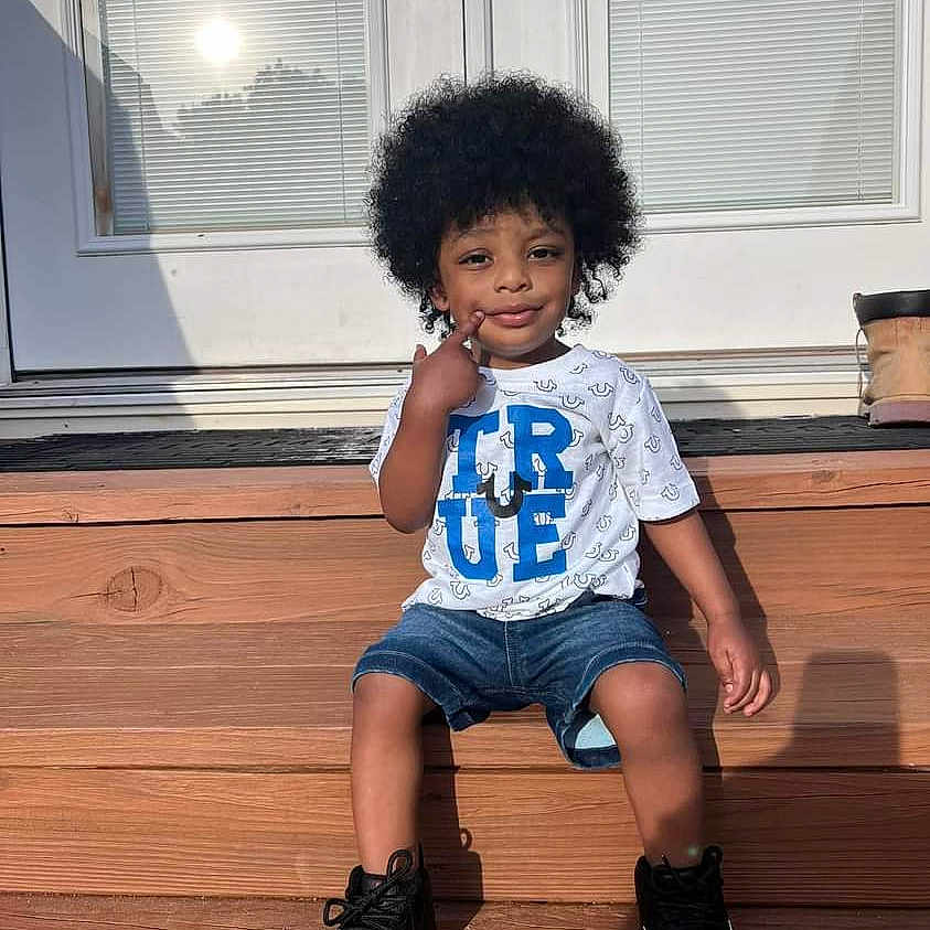 Legend joined the competition — help win amazing prizes! child, afro_hairstyle, tshirt, denim_shorts, sneakers, wooden_steps, door, sunlight, outdoor, smiling, posing, casual_clothing, young_boy, happy, person, front_door, shoes, shadow, summer, relaxed