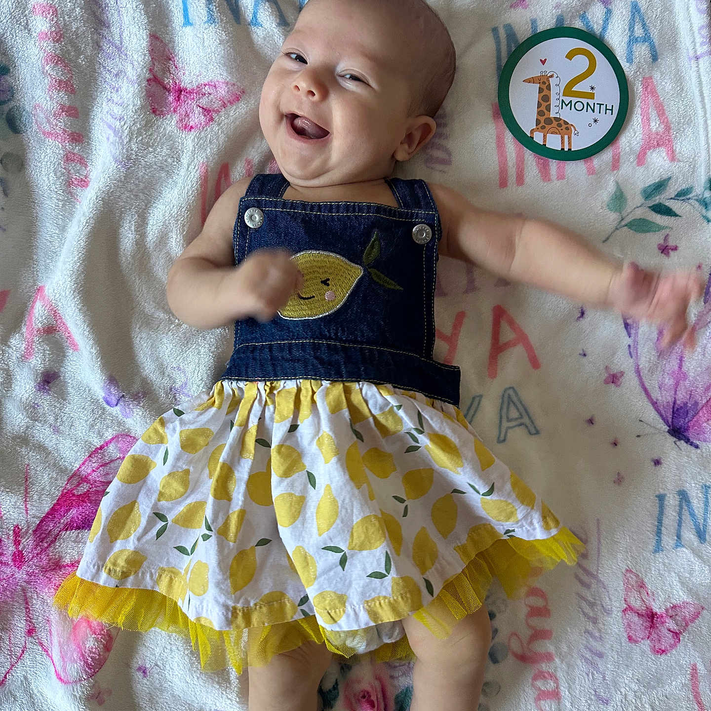 Inaya is registered to the contest to win money with this photo: baby, infant, smiling, happy, clothing, dress, denim, pattern, blanket, butterfly, giraffe, milestone, 2_month, cute, lying_down, skin, arm, head, face, person