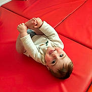 Léon participe au concours pour gagner de l'argent avec cette photo : baby, child, infant, playful, red_mat, blue_cushion, tongue_out, holding_feet, smiling, happy, indoor, soft_light, casual_clothing, head, hands, feet, cute, young_child, floor_mat, portrait