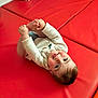 baby, child, infant, playful, red_mat, blue_cushion, tongue_out, holding_feet, smiling, happy, indoor, soft_light, casual_clothing, head, hands, feet, cute, young_child, floor_mat, portrait