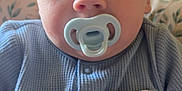 Harley is registered to the contest to win money with this photo: baby, pacifier, blue_clothing, infant, face, closeup, onesie, cute, child, portrait, sitting, indoor, cushion, pattern, soft_lighting, head, expression, young_child, comfortable, cozy