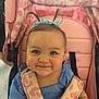 Remy is registered to the contest to win money with this photo: baby, child, smiling, blue_eyes, pigtails, bows, stroller, pink, blue_outfit, seatbelt, infant, cute, happy, portrait, indoor, person, face, clothing, seat, child_seat