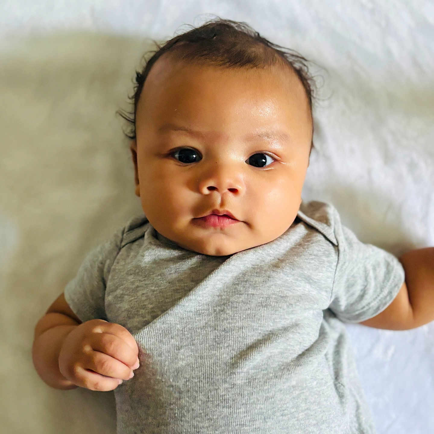 Gabriel is registered to the contest to win money with this photo: baby, infant, child, face, eyes, skin, clothing, onesie, cute, lying, portrait, expression, hand, soft, background, indoors, person, newborn, adorable, young