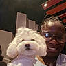 person, dog, glasses, smile, indoor, ceiling, light, hair, braids, white_dog, fluffy, pet, portrait, casual, friendship, happy, face, clothing, jewelry, background