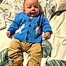 baby, infant, child, blue_sweater, polar_bear_design, tan_pants, brown_sandals, blanket, leaf_pattern, bed, lying_down, cute, curious_expression, indoors, soft_lighting, portrait, clothing, footwear, person, closeup