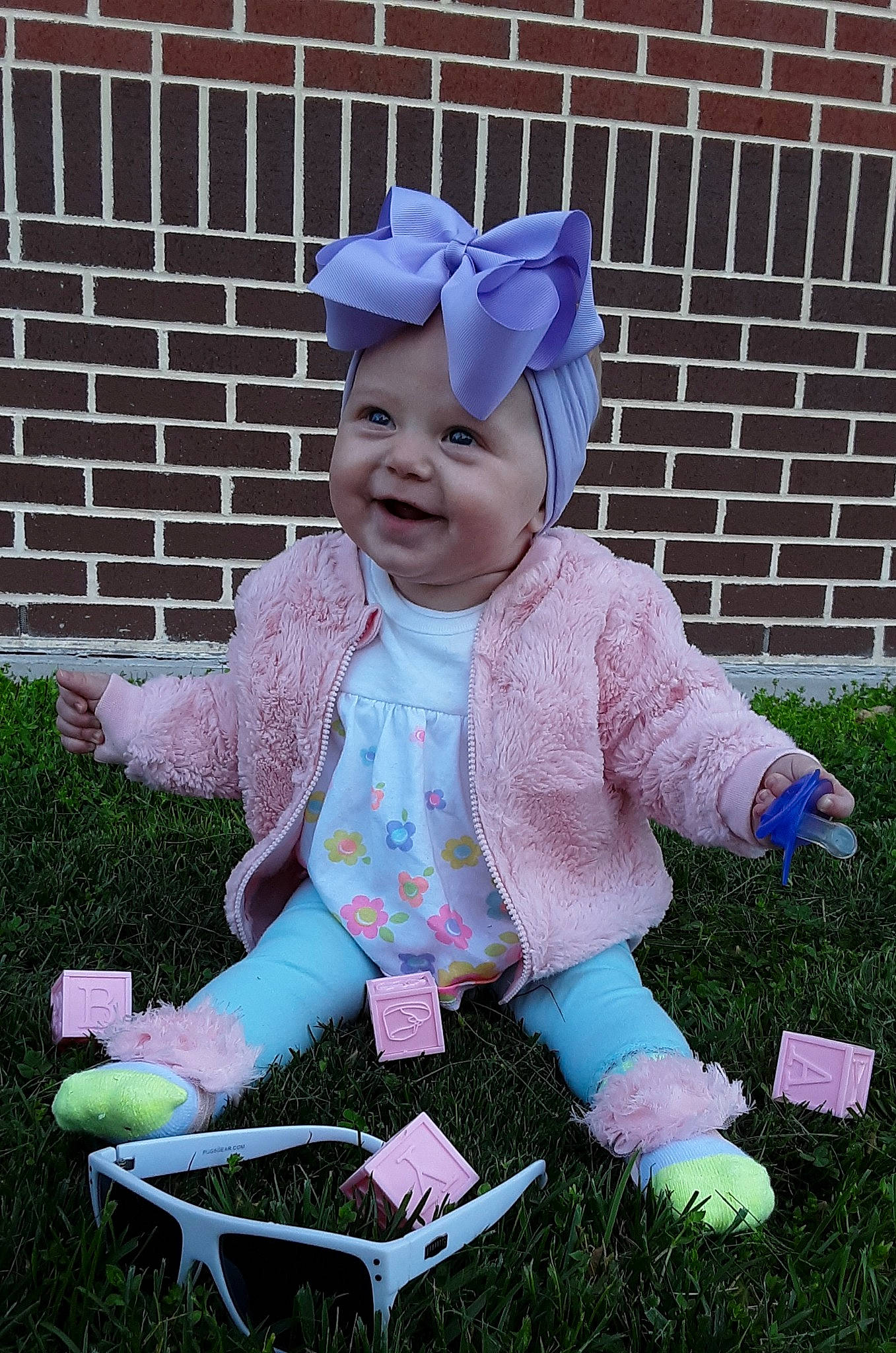 Rhea is registered to the contest to win money with this photo: baby, baby_products, baby_toddler_clothing, bonnet, child, costume, costume_accessory, grass, headgear, headwear, joy, lavender, person, pink, play, purple, sitting, smile, toddler, violet