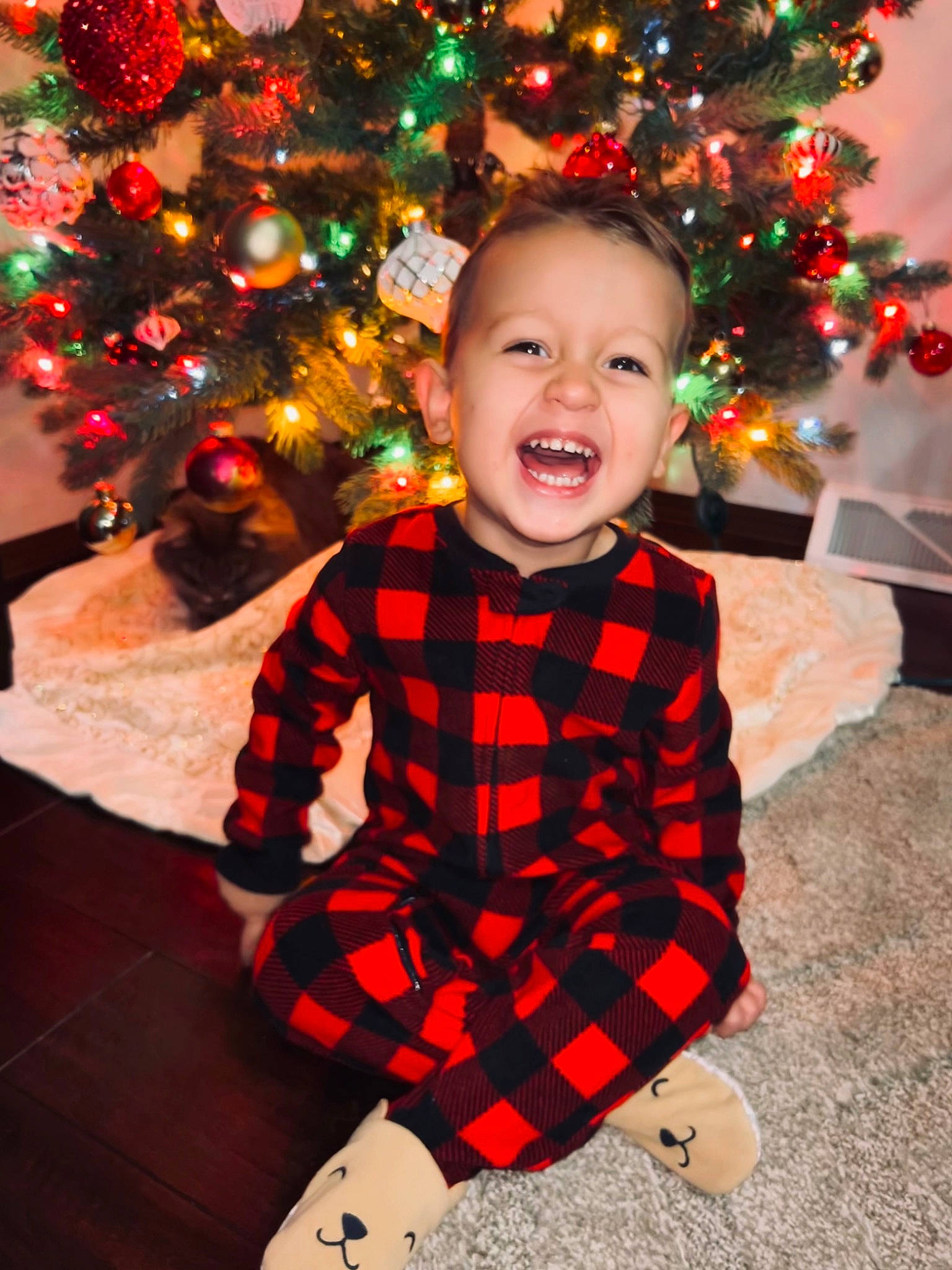 Ezrah is registered to the contest to win money with this photo: baby_toddler_clothing, christmas, christmas_decoration, christmas_ornament, christmas_tree, facial_expression, fun, happy, head, holiday, holiday_ornament, human_body, ornament, people, person, sleeve, smile, standing, toddler, tree