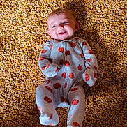 Meridith joined the competition — help win amazing prizes! baby, infant, child, smiling, happy, lying_down, portrait, face, eyes, mouth, onesie, clothing, pumpkin_pattern, red_pattern, blanket, textured_background, golden, corn_kernels, indoor, close_up