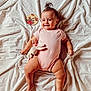 baby, infant, pink_onesie, smiling, dimples, plush_toy, bunny, pony_tail, white_sheet, milestone_card, 7_months, lying_down, happy, cute, child, skin, hand, foot, portrait, indoors