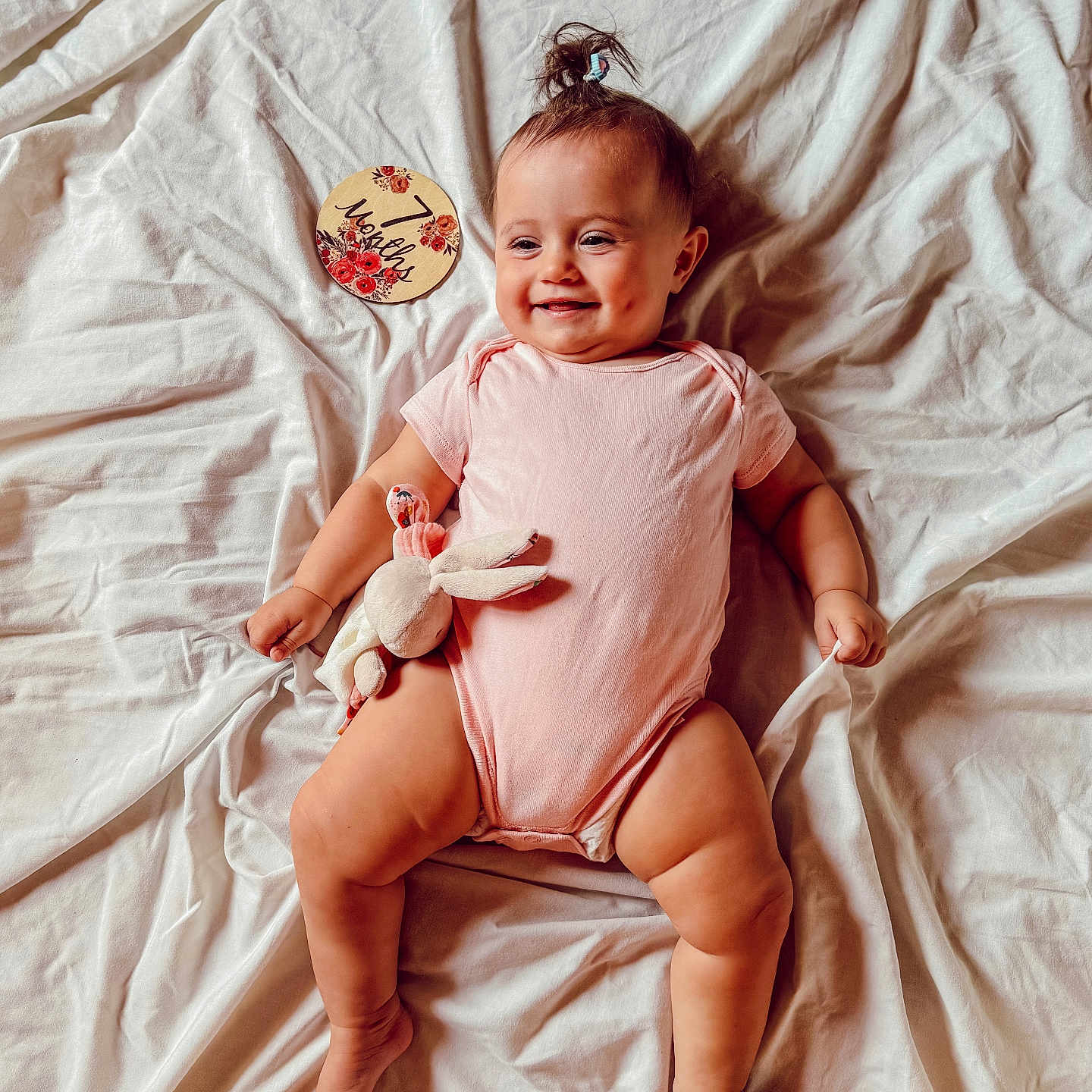 Alma a rejoint le concours — aidez-le/la à gagner de superbes lots ! 7_months, baby, bunny, child, cute, dimples, foot, hand, happy, indoors, infant, lying_down, milestone_card, pink_onesie, plush_toy, pony_tail, portrait, skin, smiling, white_sheet
