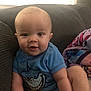 baby, child, smiling, blue_onesie, shark_design, couch, indoor, window_light, blanket, happy, infant, person, seated, cute, portrait, home, soft_light, funny_clothing, young_child, cozy