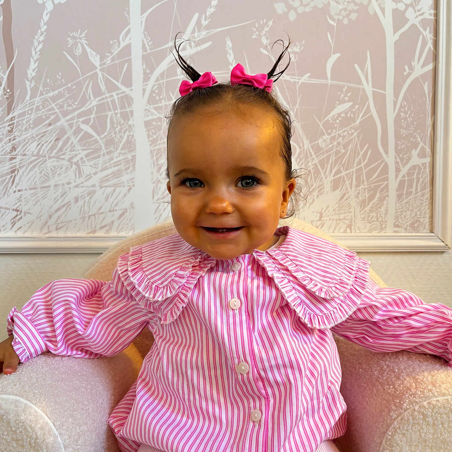Alma participe au concours pour gagner de l'argent avec cette photo : armchair, baby, buttoned_shirt, child, cozy, cute, hair_buns, happy, indoor, pastel_colors, person, pink_bows, plush_chair, portrait, ruffled_collar, sitting, smiling, striped_shirt, toddler, wallpaper