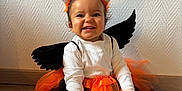 Alma participe au concours pour gagner de l'argent avec cette photo : child, costume, cute, festive, floor, halloween, happy, headband, holiday, indoor, orange_tutu, playful, portrait, sitting, smiling, toddler, wall, white_shirt, wings, witch_hat