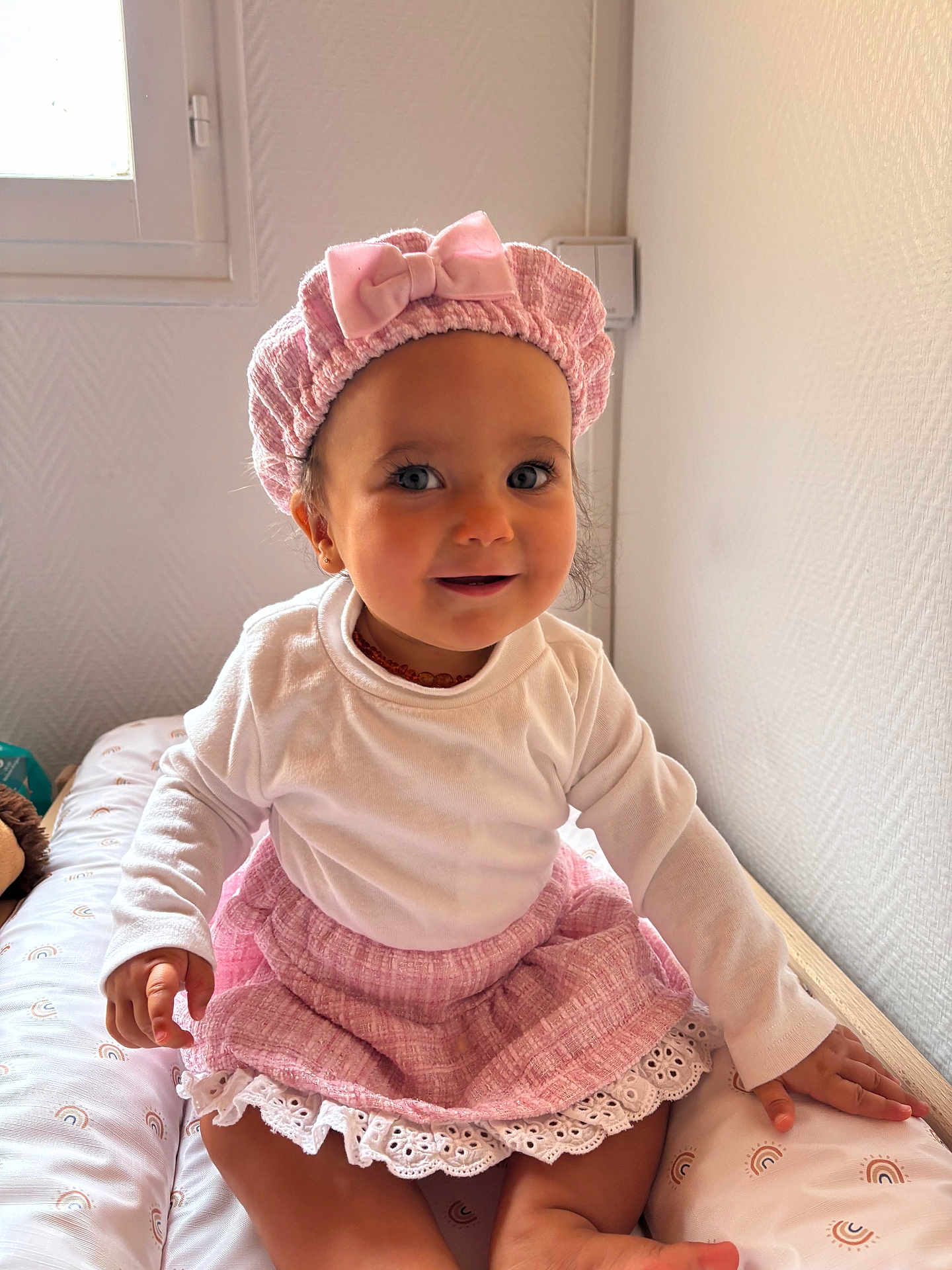 Alma participe au concours pour gagner de l'argent avec cette photo : toddler, child, baby, smiling, pink_hat, pink_skirt, white_shirt, sitting, bed, cute, indoor, portrait, happy, face, headwear, clothing, person, skin, eyes, hand