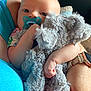 arm, baby, blue_shirt, child, closeup, clothing, comfort, cuddly, elephant_toy, face, floral_watchband, hand, indoor, infant, pacifier, person, skin, soft_toy, stuffed_animal, watch