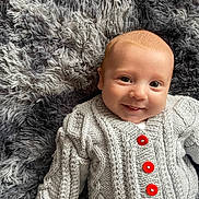 Jax joined the competition — help win amazing prizes! baby, infant, smiling, knit_sweater, red_buttons, gray_blanket, soft_texture, cute, lying_down, portrait, happy, child, young, face, cozy, warm_clothing, indoor, closeup, cable_knit, adorable