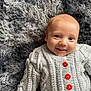 baby, infant, smiling, knit_sweater, red_buttons, gray_blanket, soft_texture, cute, lying_down, portrait, happy, child, young, face, cozy, warm_clothing, indoor, closeup, cable_knit, adorable