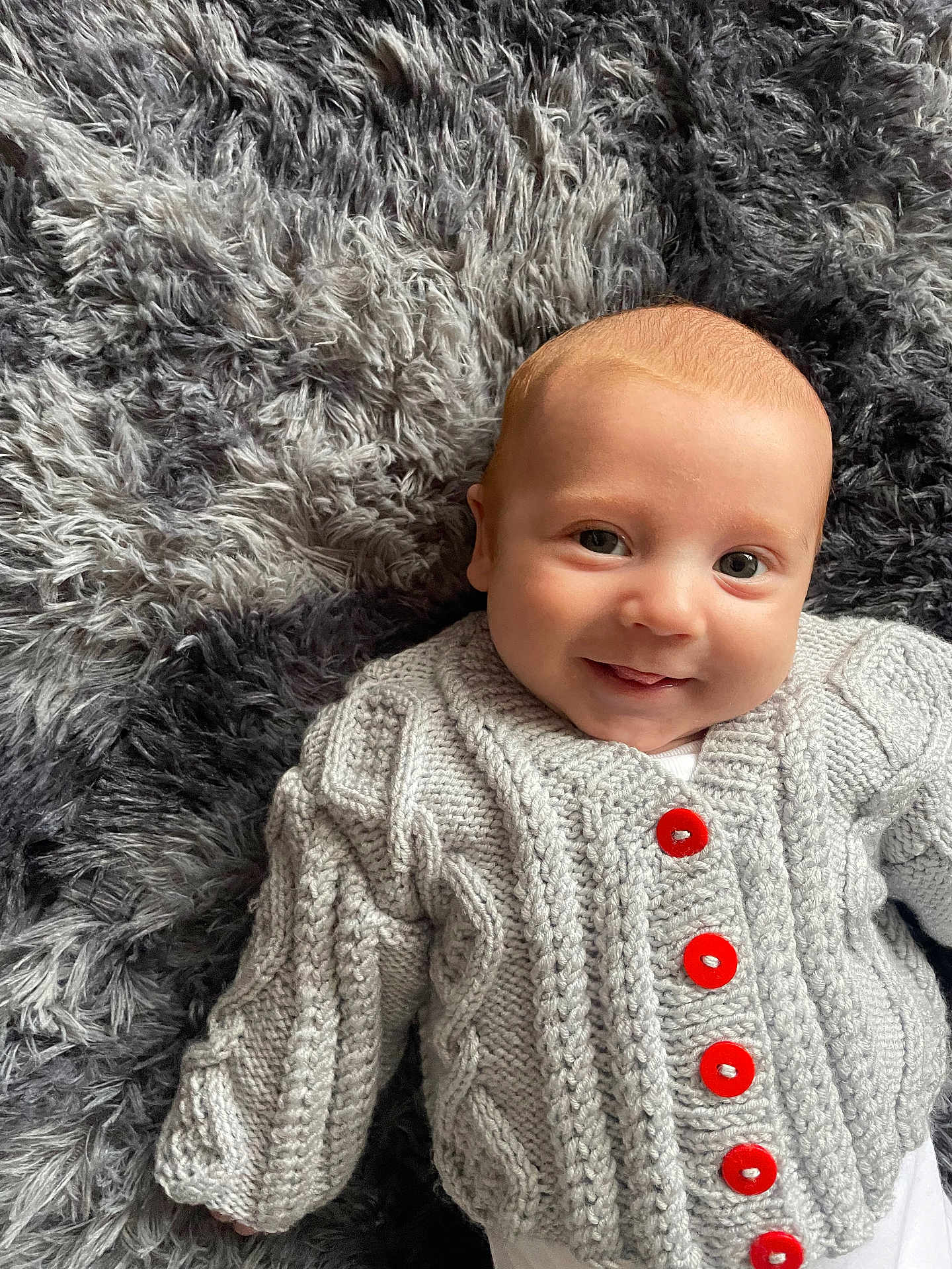Jax joined the competition — help win amazing prizes! baby, infant, smiling, knit_sweater, red_buttons, gray_blanket, soft_texture, cute, lying_down, portrait, happy, child, young, face, cozy, warm_clothing, indoor, closeup, cable_knit, adorable