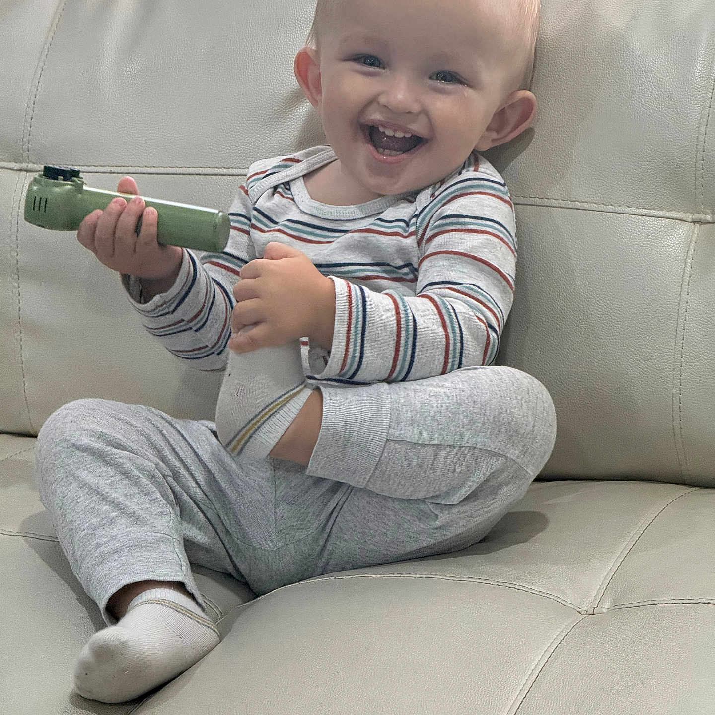 Danial is registered to the contest to win money with this photo: toddler, smiling, child, indoor, couch, toy, striped_clothing, socks, happy, sitting, leather_furniture, curtain, home, portrait, casual, playful, baby, person, young_child, cozy