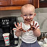 Danial is registered to the contest to win money with this photo: child, toddler, chocolate, messy, kitchen, counter, face, hands, white_shirt, blue_pants, smile, playful, cabinet, coffee_machine, cup, indoor, person, mess, food, happy
