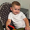 Maksym is registered to the contest to win money with this photo: background, boy, casual, child, expression, face, furniture, green_shorts, hand, high_chair, indoor, polka_dot, portrait, seated, short_hair, smartphone, smile, table, white_shirt, wooden_table