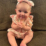 Khloe joined the competition — help win amazing prizes! baby, infant, smiling, sitting, couch, headband, bow, pink_clothing, floral_pattern, hands_clasped, barefoot, cute, portrait, indoors, child, young, face, happy, person, plush