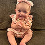 baby, infant, smiling, sitting, couch, headband, bow, pink_clothing, floral_pattern, hands_clasped, barefoot, cute, portrait, indoors, child, young, face, happy, person, plush