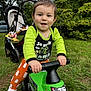 Gabriel participe au concours pour gagner de l'argent avec cette photo : toddler, child, toy_vehicle, green, outdoor, grass, stroller, trees, person, play, happy, clothing, shoes, face, hands, nature, daylight, expression, park, casual
