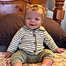 baby, child, smile, curly_hair, striped_jacket, green_pants, socks, bed, pillow, wooden_headboard, indoor, happy, cute, person, infant, portrait, seated, cozy, comfortable, home