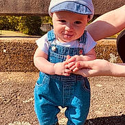 Southern is registered to the contest to win money with this photo: baby, cap, casual_clothing, child, daylight, denim_overalls, footwear, grass, happy, holding_hands, nature, outdoor, person, playful, shadow, smiling, stone_wall, sunny, support, tongue_out