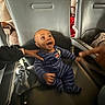Shiloh is registered to the contest to win money with this photo: baby, child, airplane_seat, seat, hand, striped_clothing, onesie, person, interior, travel, happy, smiling, infant, young_child, cabin, armrest, black_clothing, support, wide_eyes, open_mouth
