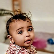 Mae'Ahna joined the competition — help win amazing prizes! adorable, baby, blurred_background, child, curious, face, hair, headshot, home, indoors, infant, looking_at_camera, patterned_clothing, photography, pink, portrait, seated, soft_lighting, topknot, wide_eyes