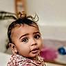 adorable, baby, blurred_background, child, curious, face, hair, headshot, home, indoors, infant, looking_at_camera, patterned_clothing, photography, pink, portrait, seated, soft_lighting, topknot, wide_eyes