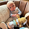 baby, child, blue_eyes, plush_toy, bunny, overalls, button, blue_shoes, leather_chair, pillow, window, natural_light, indoor, cute, infant, sitting, toy, soft_toy, cozy, portrait