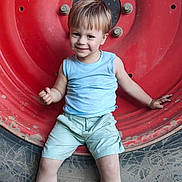 Noa a rejoint le concours — aidez-le/la à gagner de superbes lots ! child, toddler, smile, blue_shirt, shorts, sandals, tractor_tire, dirt, mud, outdoor, playful, rustic, footwear, happy, young_child, person, casual_clothing, sitting, large_tire, cute