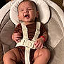 Brixton is registered to the contest to win money with this photo: baby, infant, baby_seat, seatbelt, clothing, onesie, expression, hand, legs, face, indoor, carpet, baby_gear, child, sitting, red_bracelet, comfort, cute, person, closeup