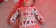 Torbin is registered to the contest to win money with this photo: baby, infant, onesie, christmas_tree, ornament, holiday, blanket, festive, red_lighting, white_tree, patterned_clothing, lying_down, cute, indoor, child, face, decorations, seasonal, celebration, newborn