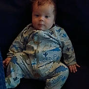 Aidan is registered to the contest to win money with this photo: baby, infant, child, dinosaur_onesie, onesie, sitting, chair, indoor, portrait, face, eyes, red_hair, wide_eyed, hands, feet, dark_background, furniture, cute, casual_clothing, photograph
