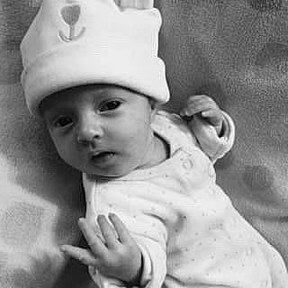 Elise is registered to the contest to win money with this photo: art, baby, baby_toddler_clothing, black_and_white, cap, cheek, child, comfort, fashion_accessory, gesture, happy, headgear, headwear, monochrome, monochrome_photography, person, portrait_photography, sitting, skin, sleeve