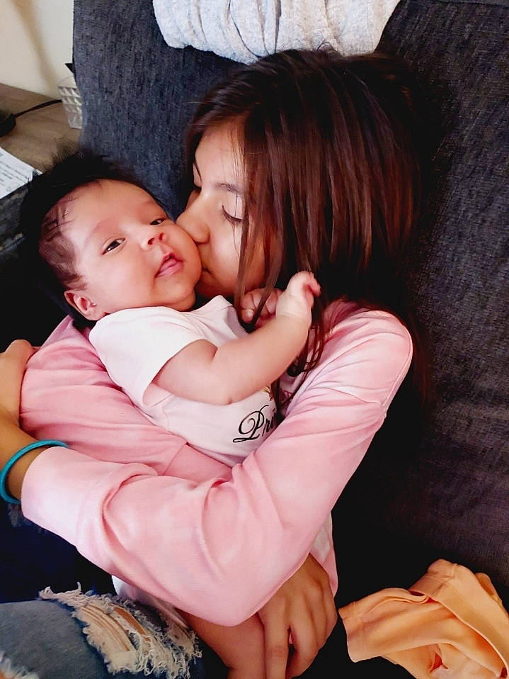 Kamila is registered to the contest to win money with this photo: abdomen, arm, baby, baby_toddler_clothing, cheek, comfort, elbow, event, finger, flash_photography, fun, gesture, happy, hug, interaction, lap, person, plant, sitting, smile