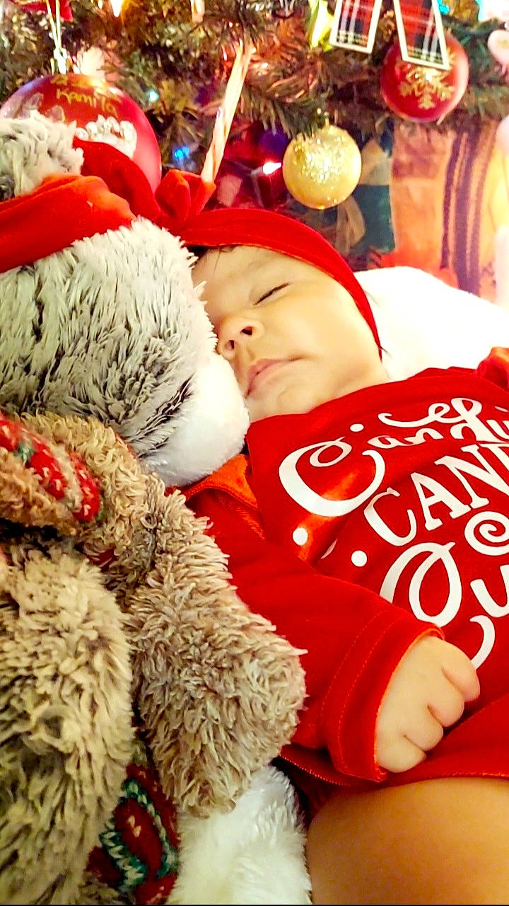 Kamila is registered to the contest to win money with this photo: baby, baby_toddler_clothing, cap, comfort, event, facial_expression, fur_clothing, happy, hat, head, headgear, headwear, human_body, interaction, linens, person, santa_claus, stuffed_toy, teddy_bear, toddler