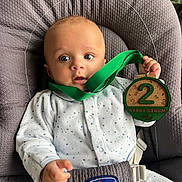 Léonard participe au concours pour gagner de l'argent avec cette photo : baby, infant, onesie, baby_seat, chicco, medal, green_ribbon, wooden_medal, face, blue_eyes, hand, clothing, indoor, cute, child, expression, comfort, sitting, young_child, portrait