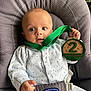 baby, infant, onesie, baby_seat, chicco, medal, green_ribbon, wooden_medal, face, blue_eyes, hand, clothing, indoor, cute, child, expression, comfort, sitting, young_child, portrait