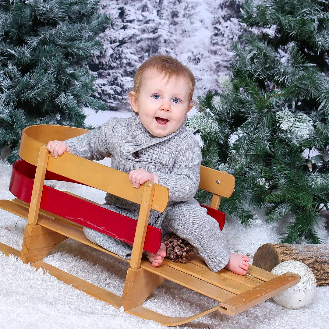 Lola is registered to the contest to win money with this photo: baby_toddler_clothing, chair, child, christmas_tree, comfort, conifer, event, fun, grass, holiday, human_body, ornament, outdoor_furniture, person, sitting, smile, snow, toddler, tree, winter