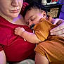 baby, child, adult, sleeping, holding, hand, red_shirt, orange_clothing, indoor, closeup, face, curly_hair, pacifier, skin, comfort, rest, caring, person, nail_polish, furniture