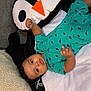 baby, child, dinosaur_print, onesie, plush_toy, penguin, blanket, pillow, indoor, carpet, infant, cute, toddler, lying_down, clothing, face, expression, hand, soft_toy, portrait