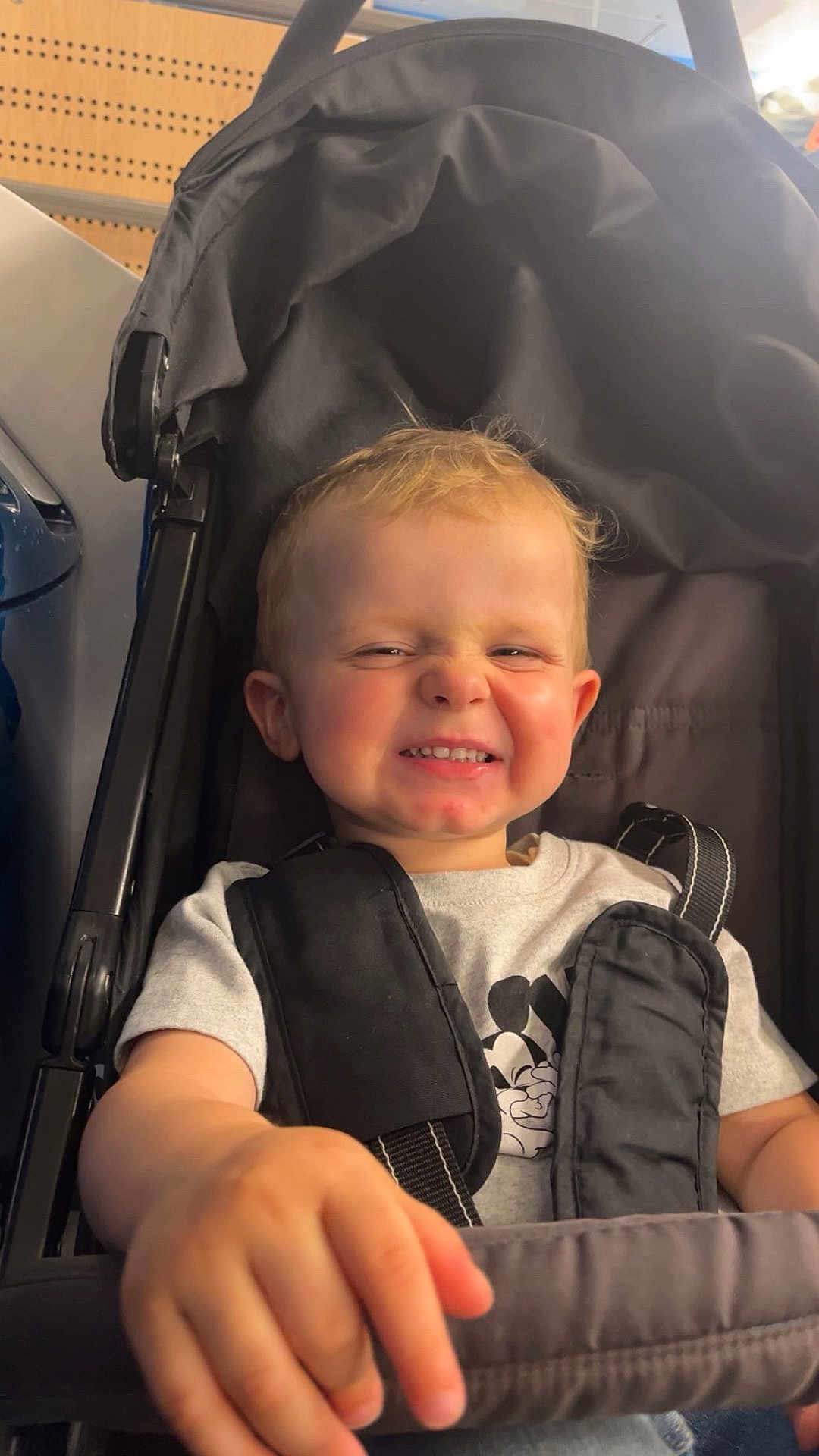 Rafaël participe au concours pour gagner de l'argent avec cette photo : toddler, child, smile, grin, stroller, seatbelt, mickey_mouse, tshirt, indoor, light, hand, person, cute, expression, face, hair, clothing, seat, happy, young