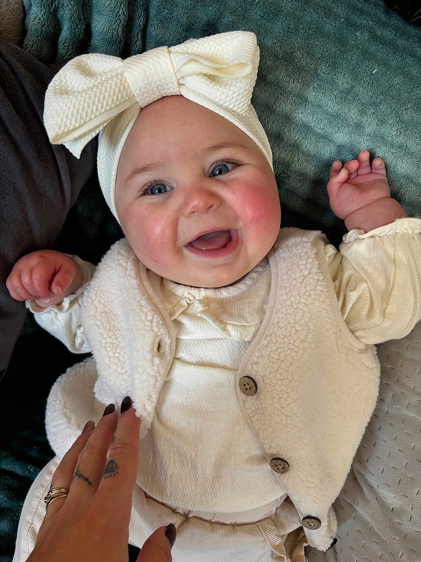Adrya participe au concours pour gagner de l'argent avec cette photo : baby, infant, headband, bow, smile, rosy_cheeks, blue_eyes, vest, buttons, onesie, hand, adult_hand, ring, tattoo, blanket, fabric_texture, portrait, closeup, happy, indoor
